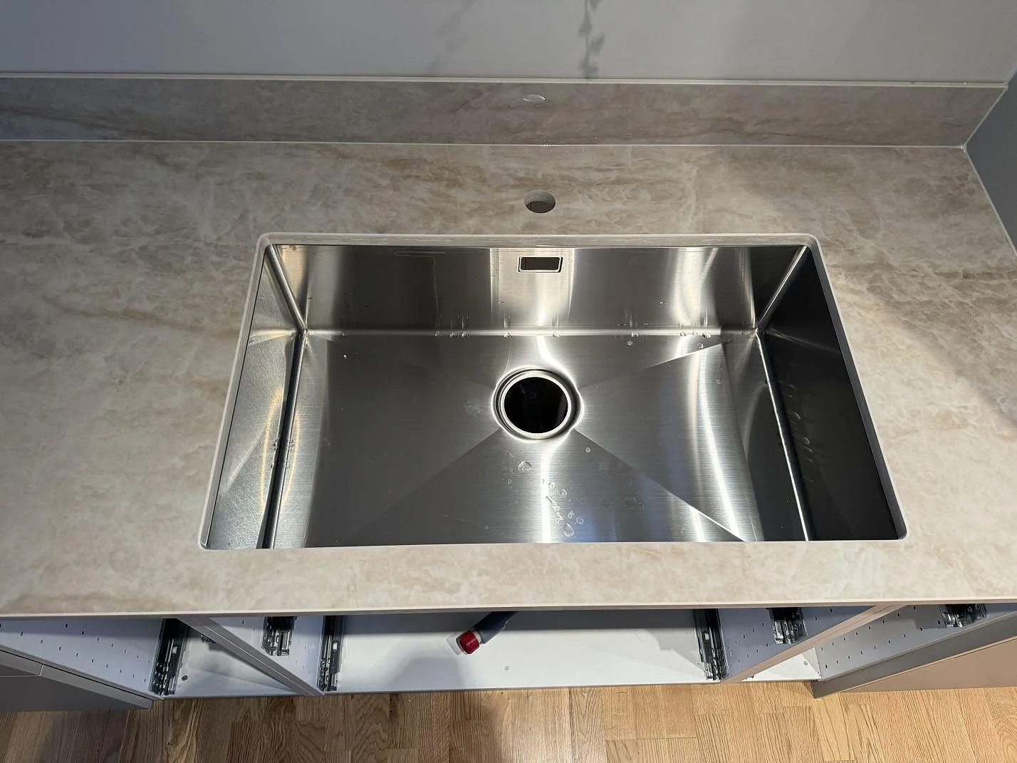 Närbild ovanifrån på rostfri diskho monterad under polerad Dekton Arga med beige ådring och stänkskydd i Mölndal.