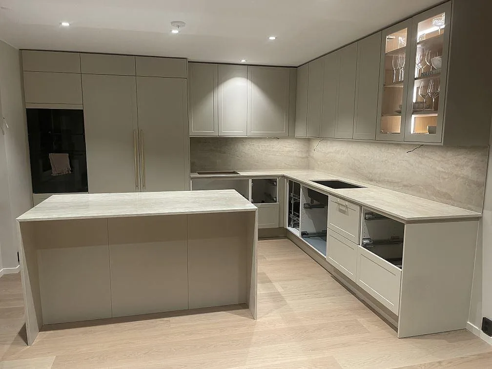 Köksbänkskiva i ljus Dekton Arga, polerad, i ett U-format kök med köksö och heltäckande stänkvägg i sten i Norsborg.