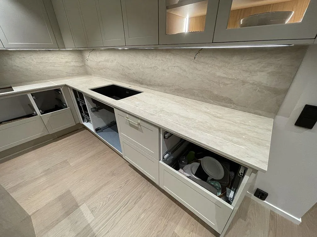 Polerad Dekton Arga bänkskiva längs L-delen med köksö och svart underlimmad diskho i ett kök i Norsborg.