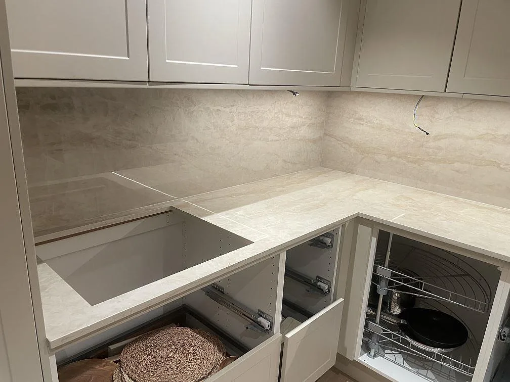 Hörnparti av Dekton Arga köksbänkskiva med diskhourtag och stänkvägg i sten under montering i Norsborg.