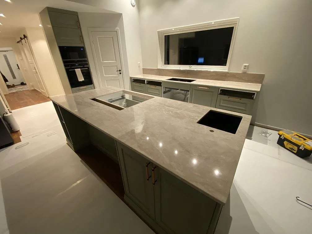 Köksö i Dekton Arga med urfräsning för häll och underlimmad diskho, eye-level-vy över hela köket i Nybro under montering.