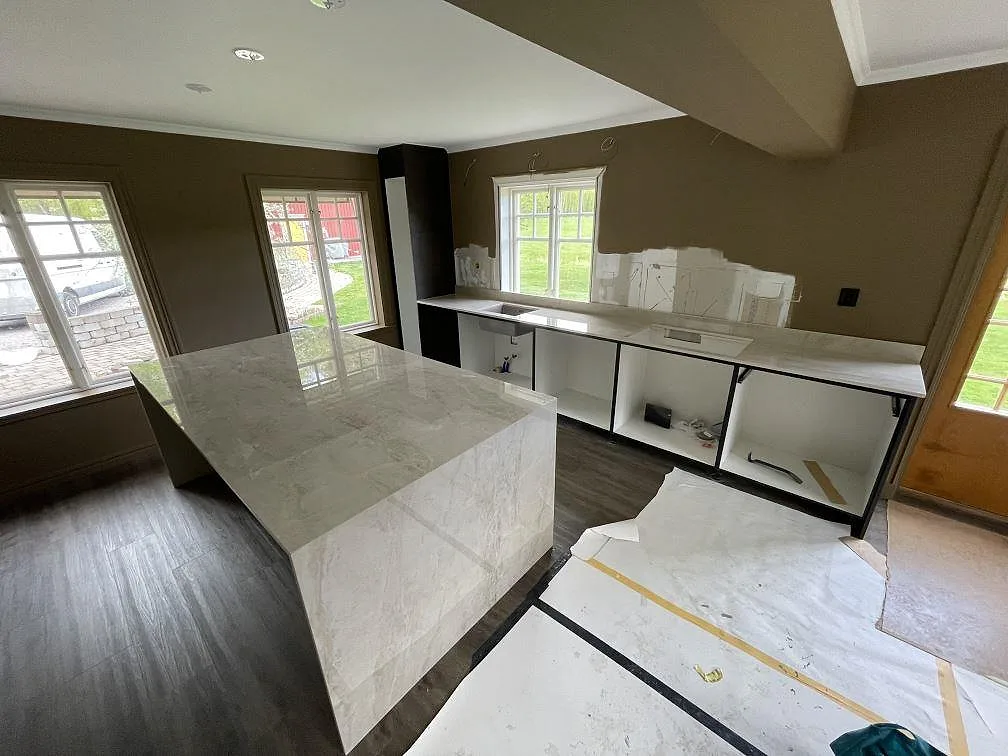 Köksbänkskiva och köksö i ljusgrå Dekton Arga, polerad keramik med marmorlik ådring, monterad i ett kök under installation i Sala.
