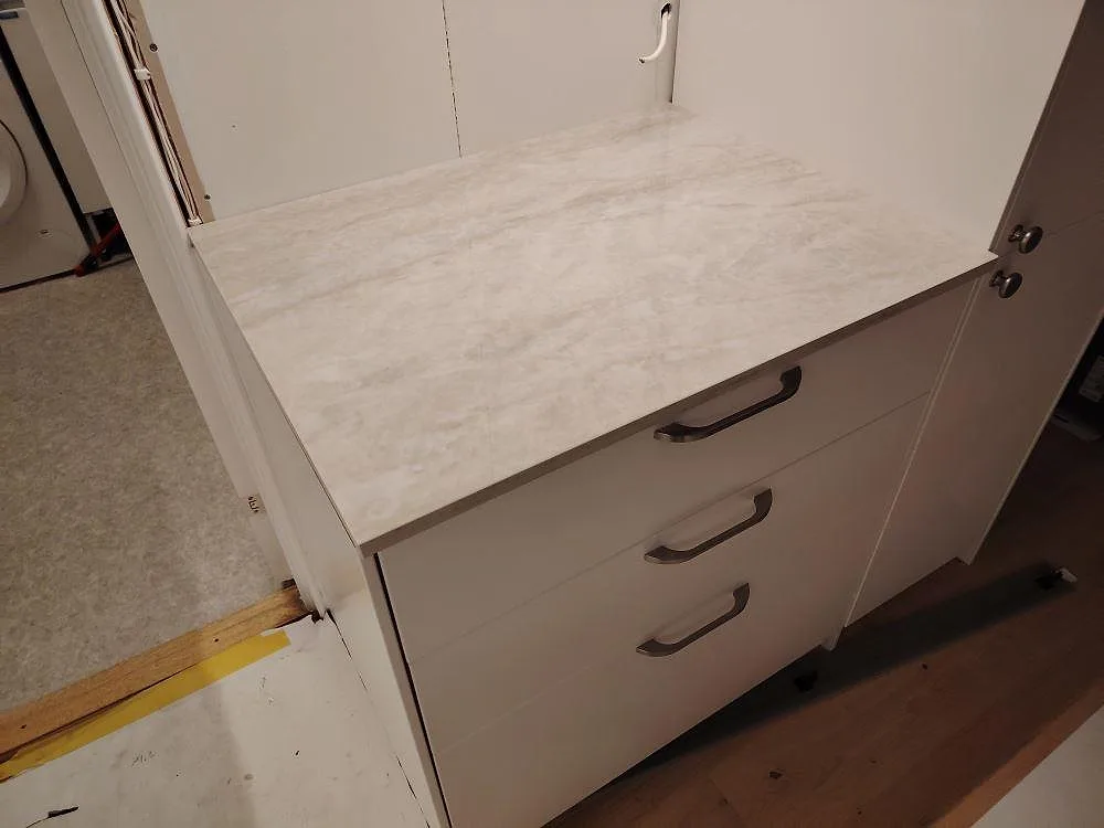 Närbild på separat köksbänkskiva i polerad Dekton Arga, ljus keramik med mjuk ådring, monterad på lådor i Saltsjö Boo.