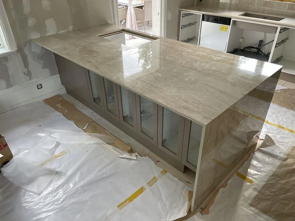 Köksö i polerad Dekton Arga keramik med förberedd hällöppning och neddragen sidopanel under montering i Sandviken.