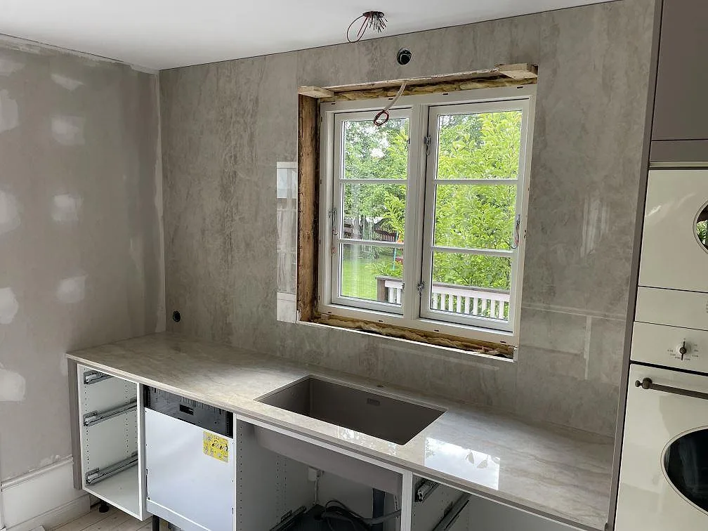 Diskzon i polerad Dekton Arga med bänkskiva, rektangulär diskho och hög väggbeklädnad runt fönstret i Sandviken.