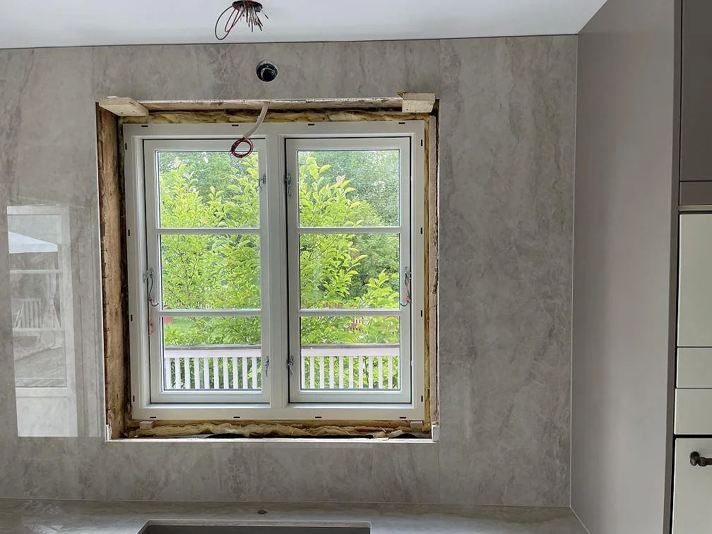 Hög väggbeklädnad i polerad Dekton Arga runt köksfönster, med bänkskivan synlig nedtill i Sandviken.