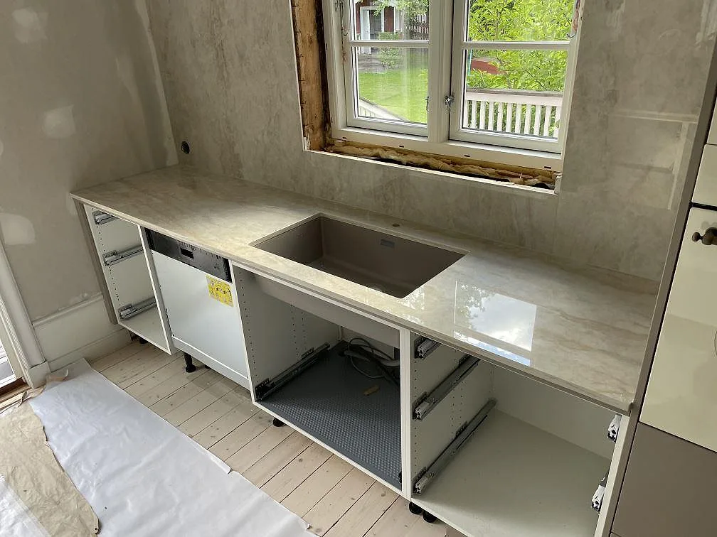 Rak köksbänkskiva i polerad Dekton Arga med diskho vid fönster och matchande väggbeklädnad i ett kök i Sandviken.