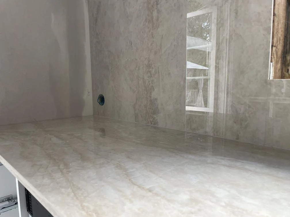 Detalj av polerad Dekton Arga med ljus ådring på bänkskiva och väggbeklädnad i köket i Sandviken.