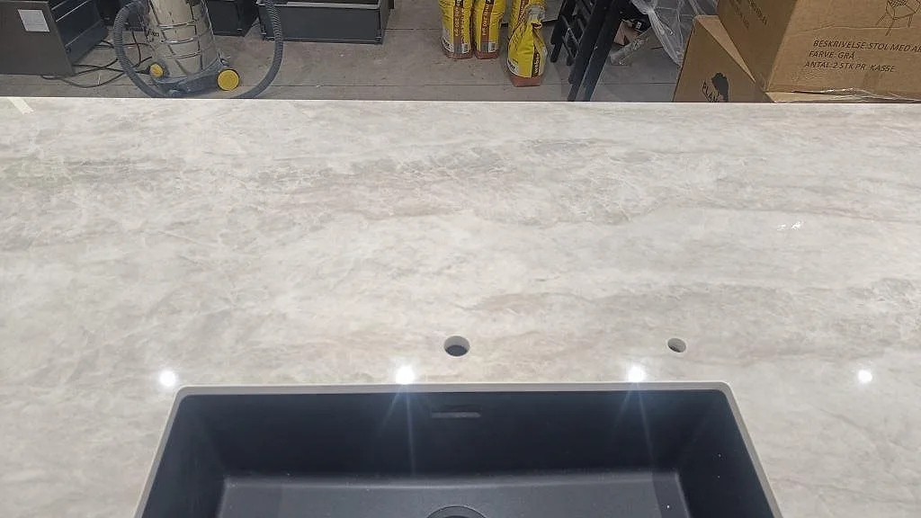 Ytbild av polerad Dekton Arga med blandarhål, diskho och tydlig beigegrå ådring i köket i Sengeløse.
