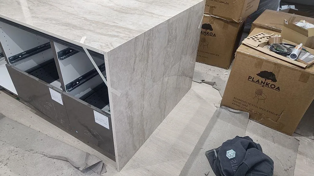 Sidovy av köksö i Dekton Arga med neddragen gavel, polerad sten och mörka stommar under montering i Sengeløse.