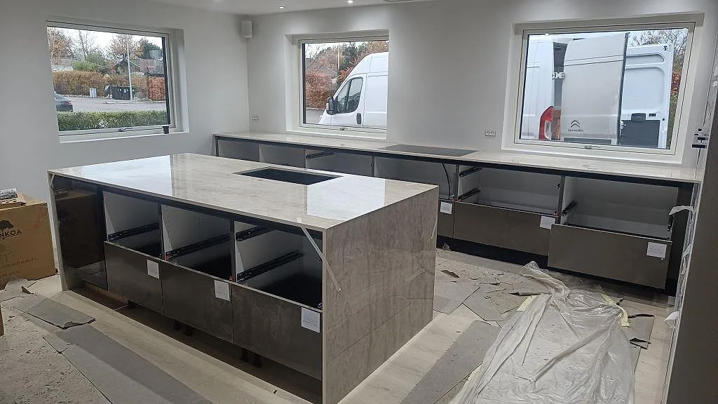 Köksbänkskiva och stor köksö i polerad Dekton Arga med ljus ådring, mörka stommar och stora fönster i Sengeløse.