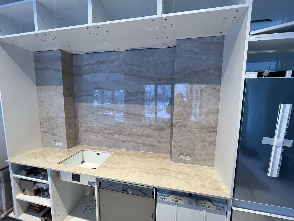 Väggbänk och höga stänkpaneler i polerad Dekton Arga med ho och kyl i ett kök under montering i Sigtuna.