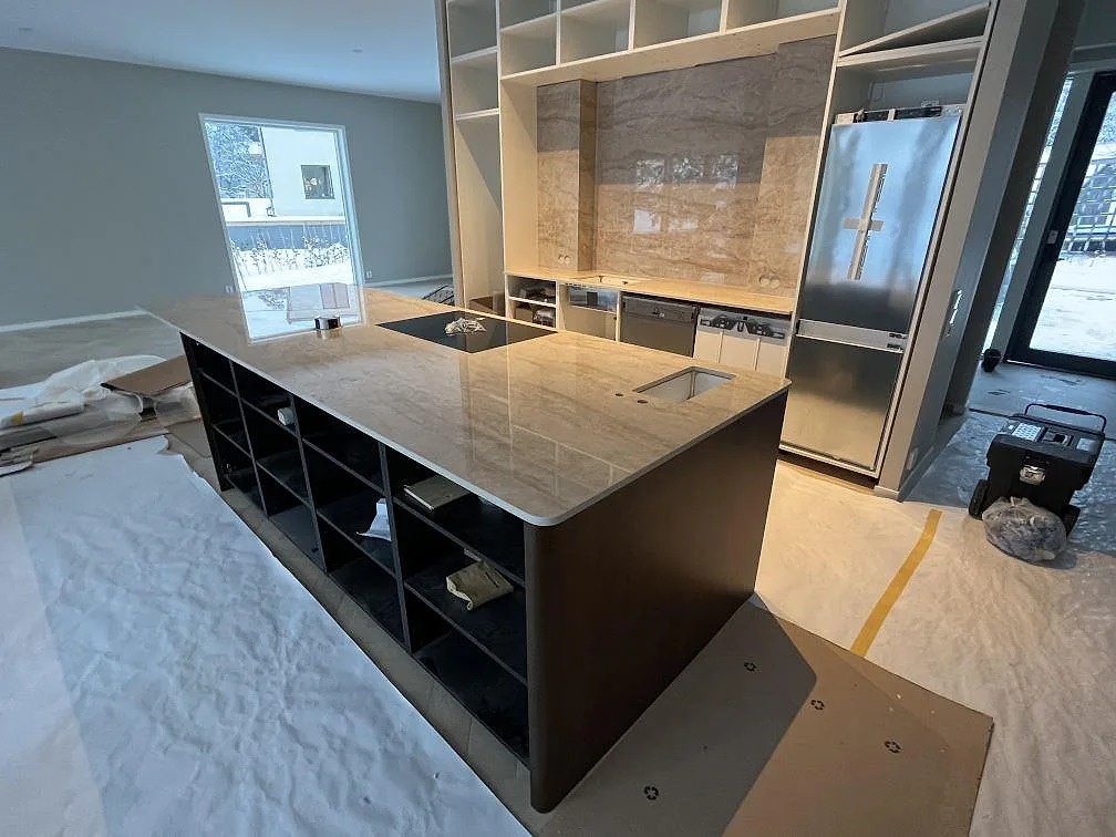 Köksö och köksbänkskiva i polerad Dekton Arga med beige ådring, häll och ho i ett kök under montering i Sigtuna.