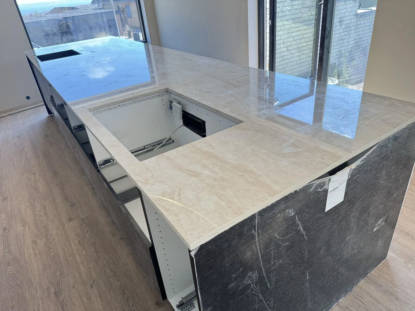 Köksbänkskiva i polerad Dekton Arga, keramik, med öppna köksstommar och utskärningar under montering i Skødstrup.