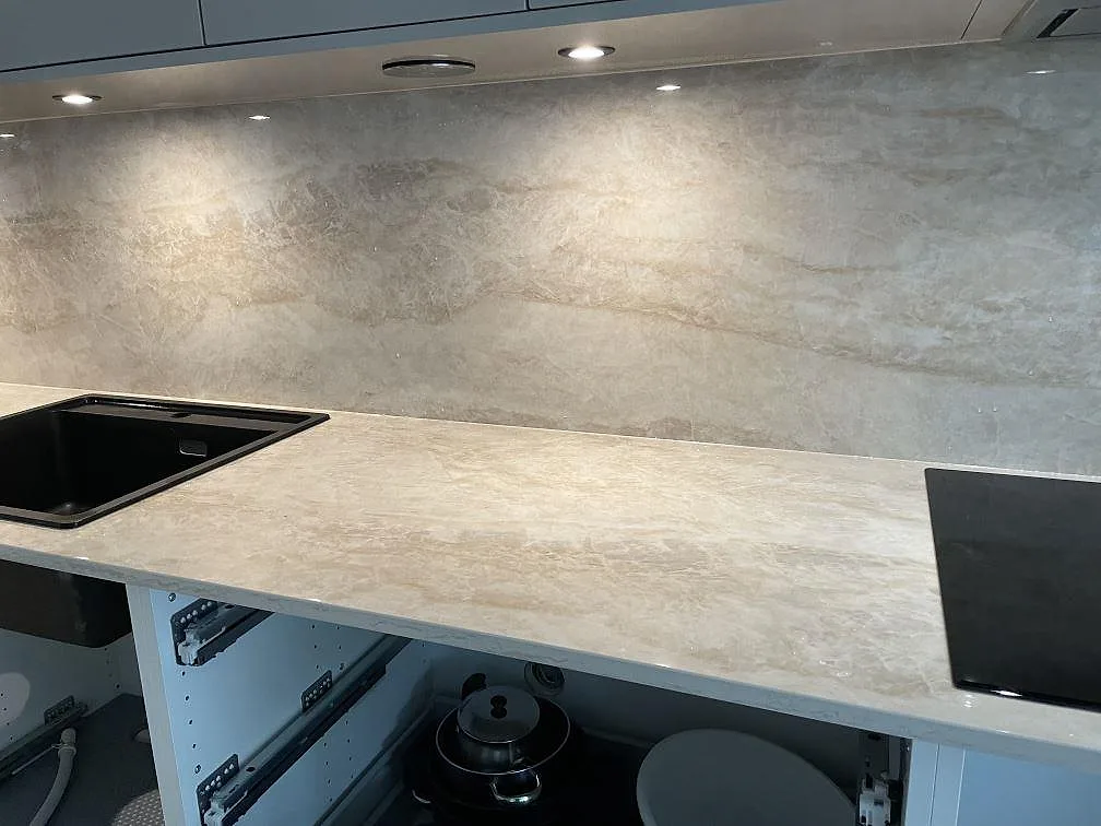 Köksbänk i polerad Dekton Arga med svart diskho, svart häll och hög stänkskiva i sten i Skövde.