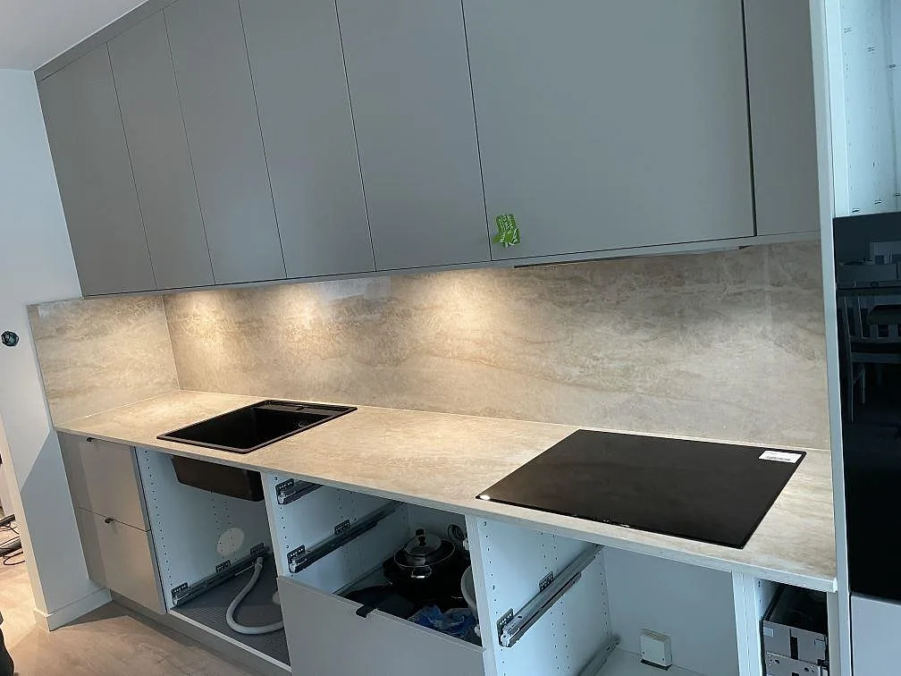 Köksbänkskiva i polerad Dekton Arga med svart diskho, svart häll och fullhöjd sten bakom arbetsytan i ett kök i Skövde.