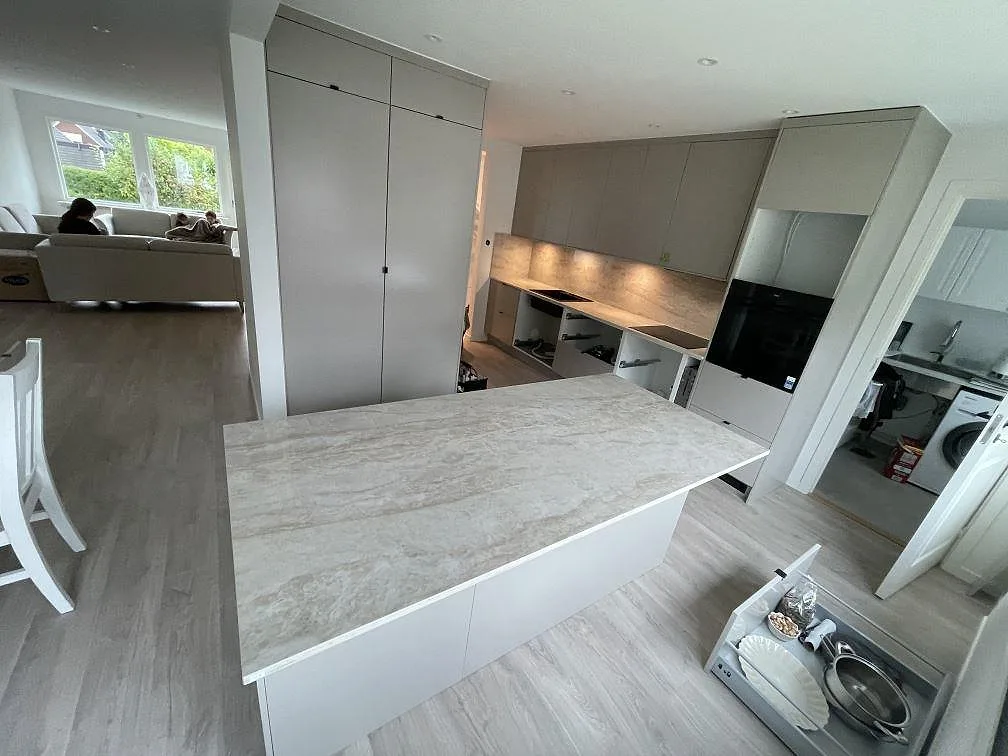 Polerad Dekton Arga som köksö och L-formad köksbänk i ett ljust kök under montering i Skövde.