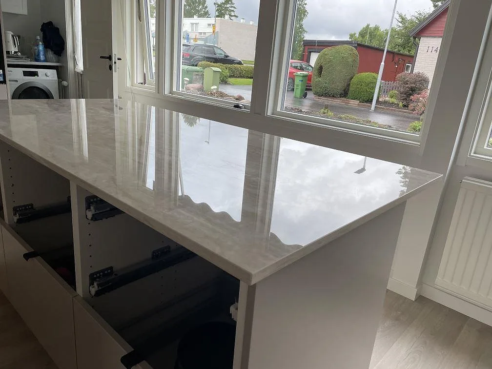 Köksö i polerad Dekton Arga med travertinlik ådring och stora fönster i ett kök i Skövde.