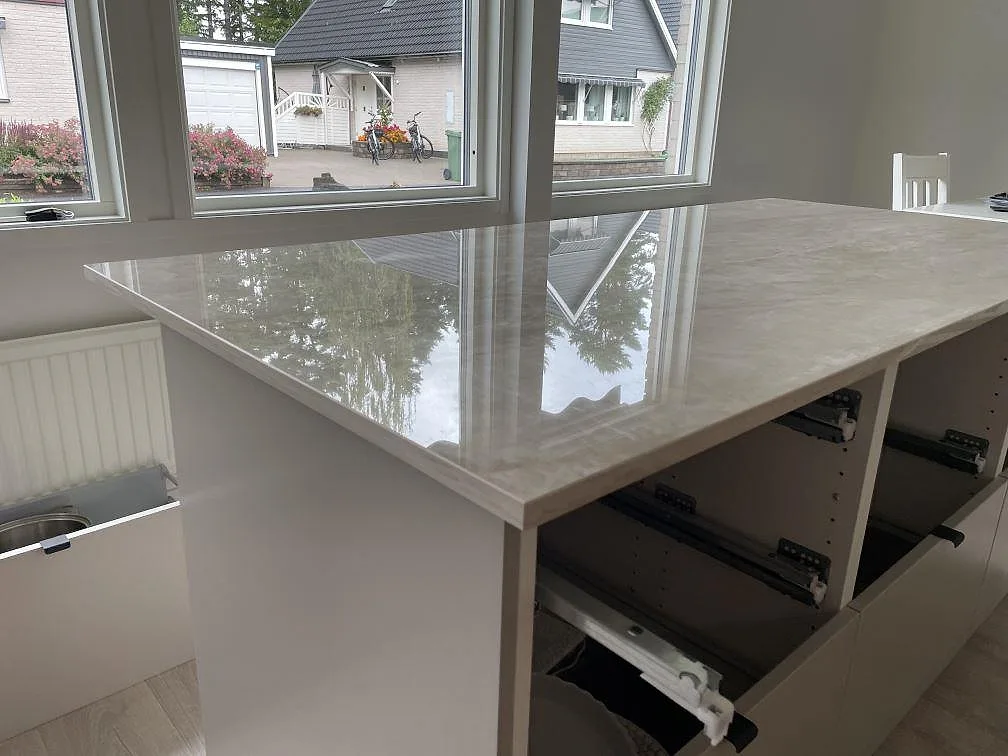 Blank köksö i Dekton Arga keramik med ljusa reflexer från fönster och öppna köksstommar i Skövde.
