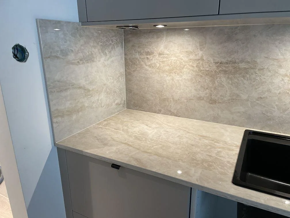 Detalj av polerad Dekton Arga som bänkskiva och fullhöjd stänkskiva med svart diskho i ett kök i Skövde.