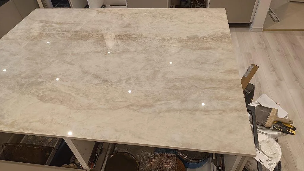 Detalj av polerad Dekton Arga på köksön, med ljusreflexer och verktyg bredvid arbetsytan i Skövde.