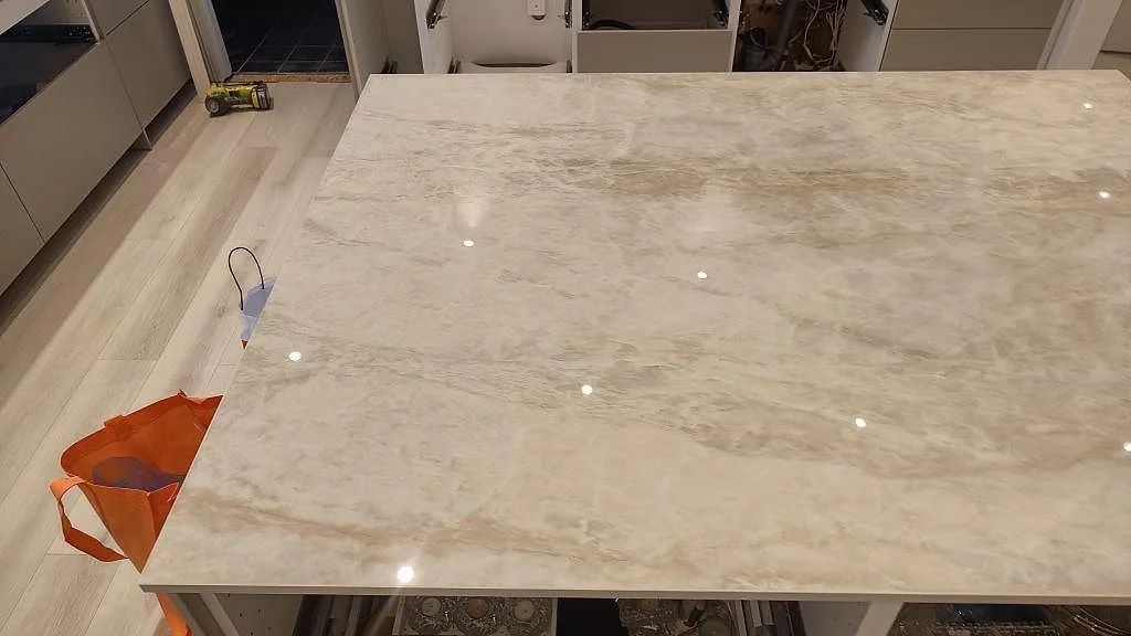 Översiktsbild över köksön i polerad Dekton Arga, där den varma ådringen syns under montering i Skövde.