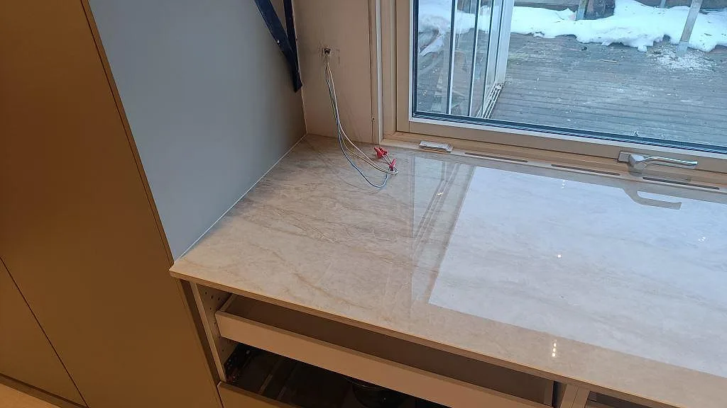 Sidovy av fönsterbänksdelen i polerad Dekton Arga, monterad över öppna köksstommar i Skövde.