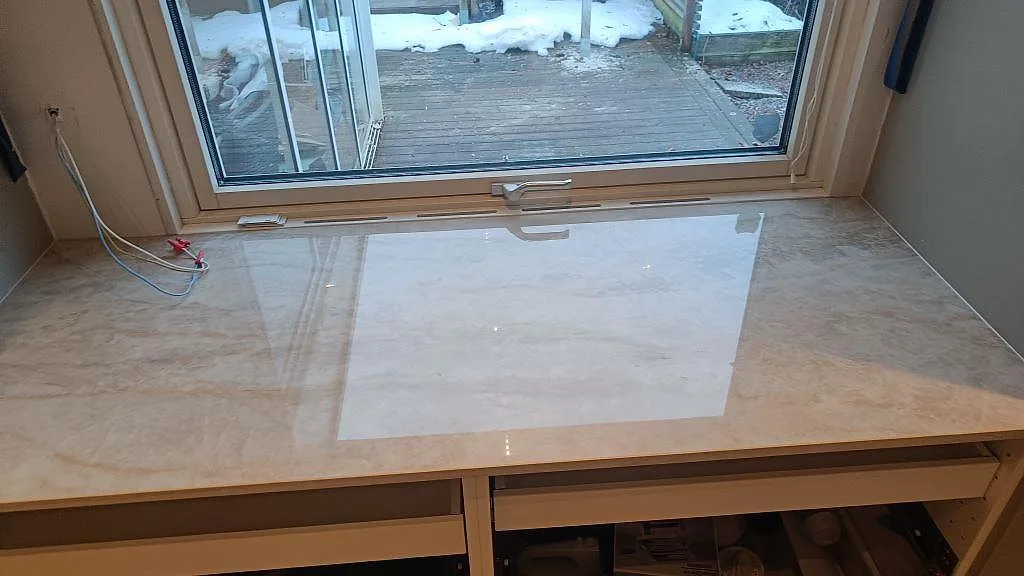 Bänkrad vid fönster i polerad Dekton Arga med ljus ådring och reflektion från fönstret i Skövde.