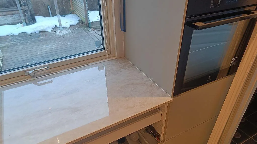 Polerad Dekton Arga vid fönster och högskåp, med beige keramikyta och monterad bänkrad i Skövde.