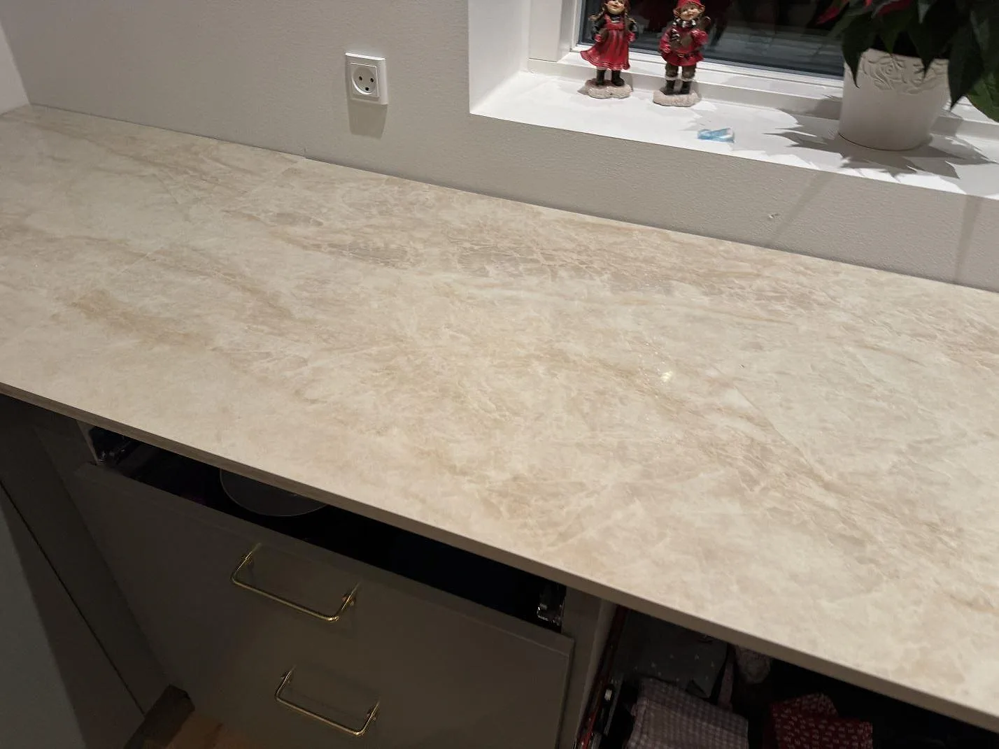 Lång köksbänkskiva i krämig Dekton Arga keramik som löper fram mot ett fönster i ett kök i Skovlunde, polerad yta.