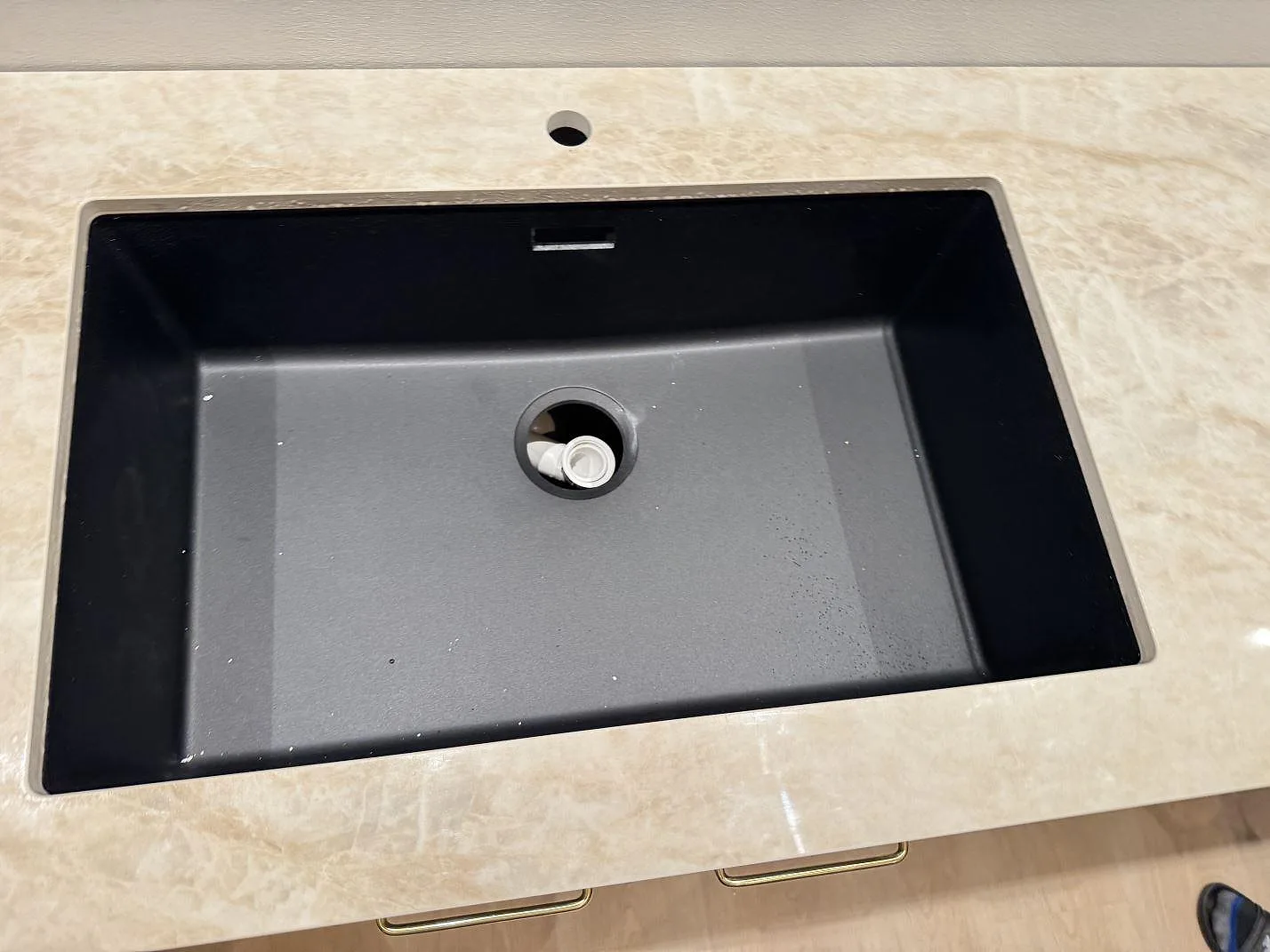 Närbild ovanifrån på en svart underlimmad diskho infälld i en polerad köksbänkskiva i beige Dekton Arga keramik i Skovlunde.