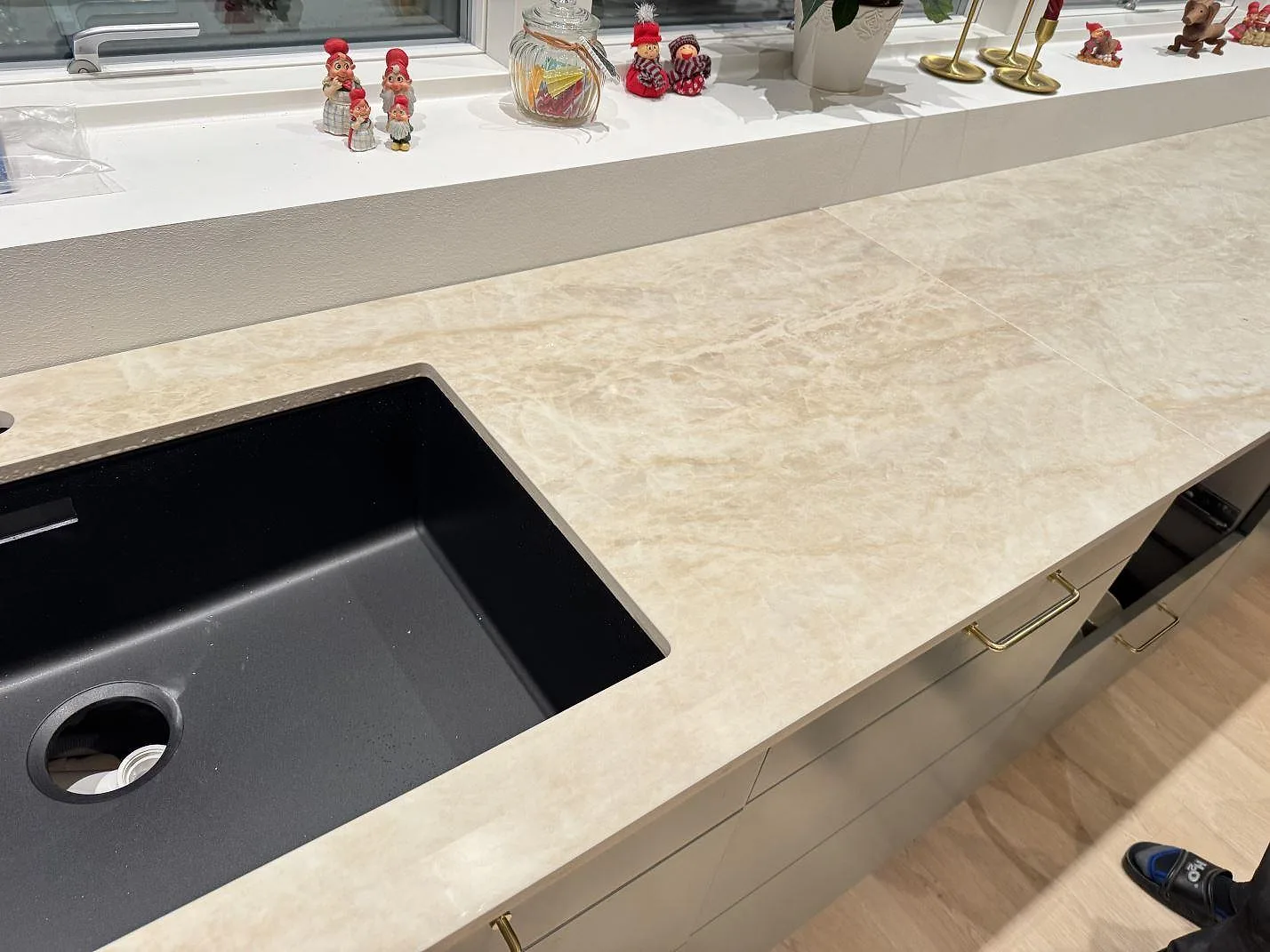 Köksö och bänkskiva i beige Dekton Arga med den svarta kompositdiskhon i en vinklad vy i ett kök i Skovlunde.