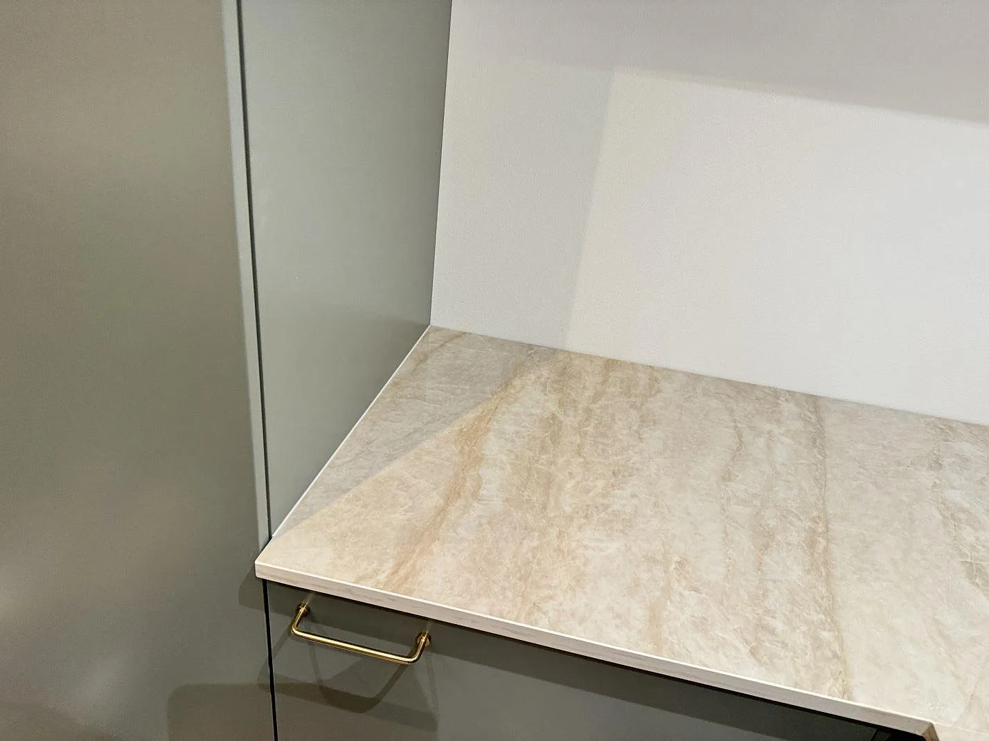 Polerad köksbänkskiva i beige Dekton Arga med mjukt rinnande ådring mot ett stänkskydd och en hög skåpsida i ett kök i Skovlunde.