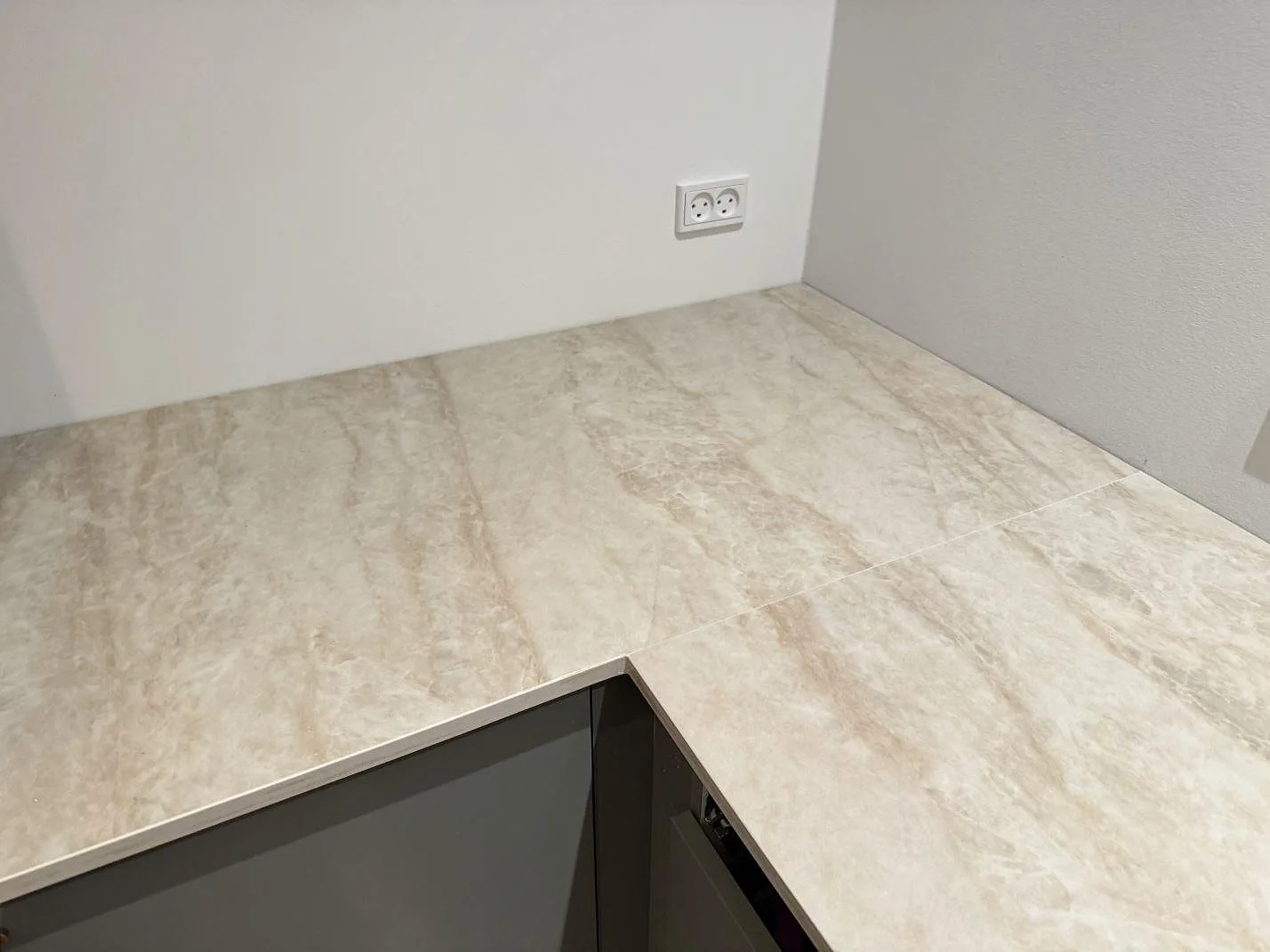 Köksbänkskiva i polerad Dekton Arga keramik i vinkel med synlig skarv och ådring längs väggen i ett kök i Skovlunde.