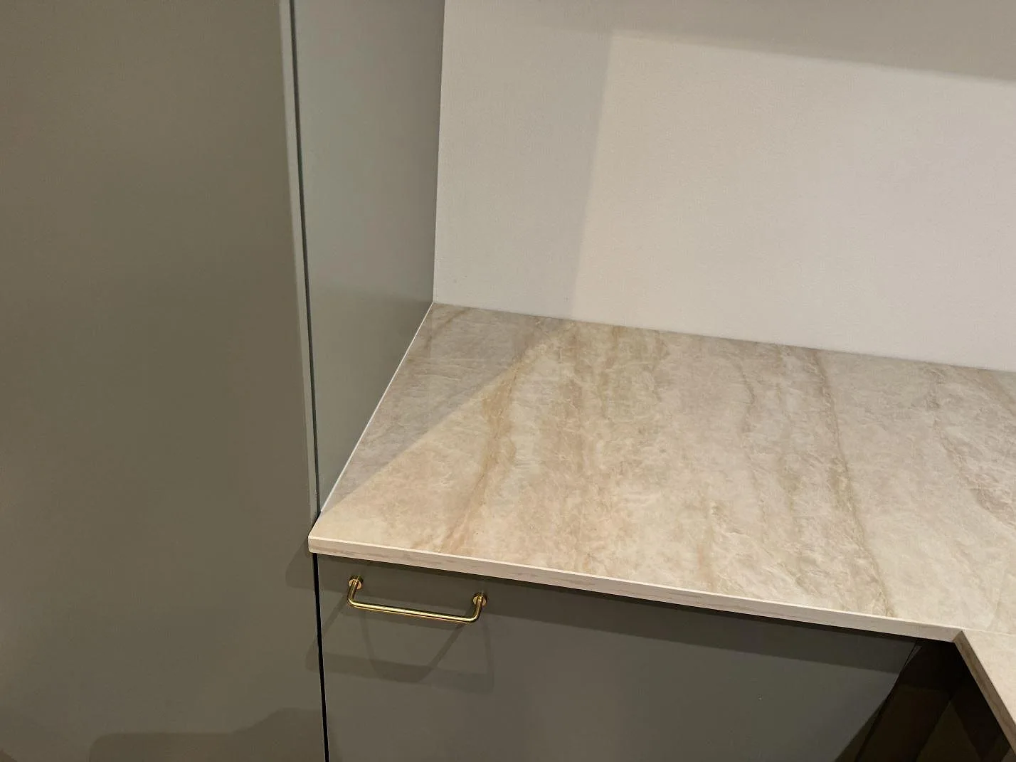 Hörn av en köksbänkskiva i polerad Dekton Arga keramik mot ett vitt stänkskydd, med ljus beige ådring i ett kök i Skovlunde.