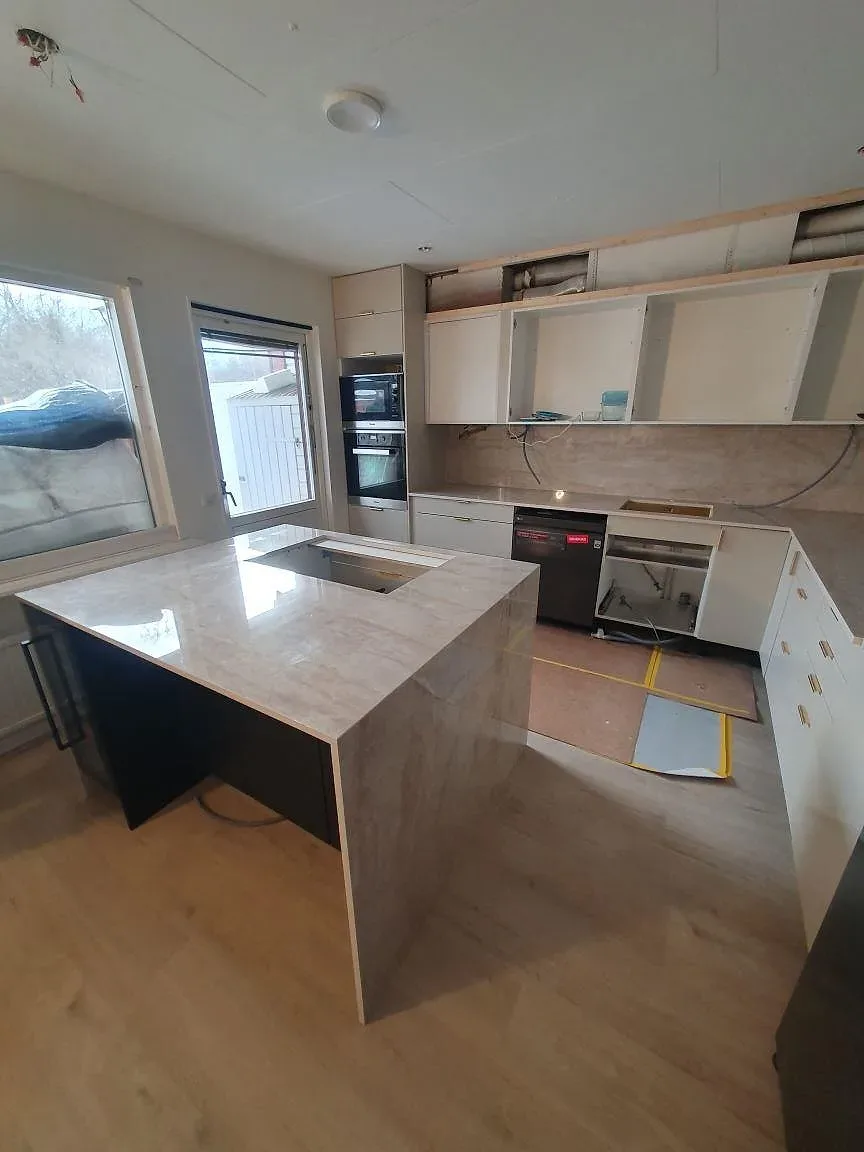Stor köksö i polerad Dekton Arga keramik med hällurtag, vit köksinredning och ljus ådring i Söderby.