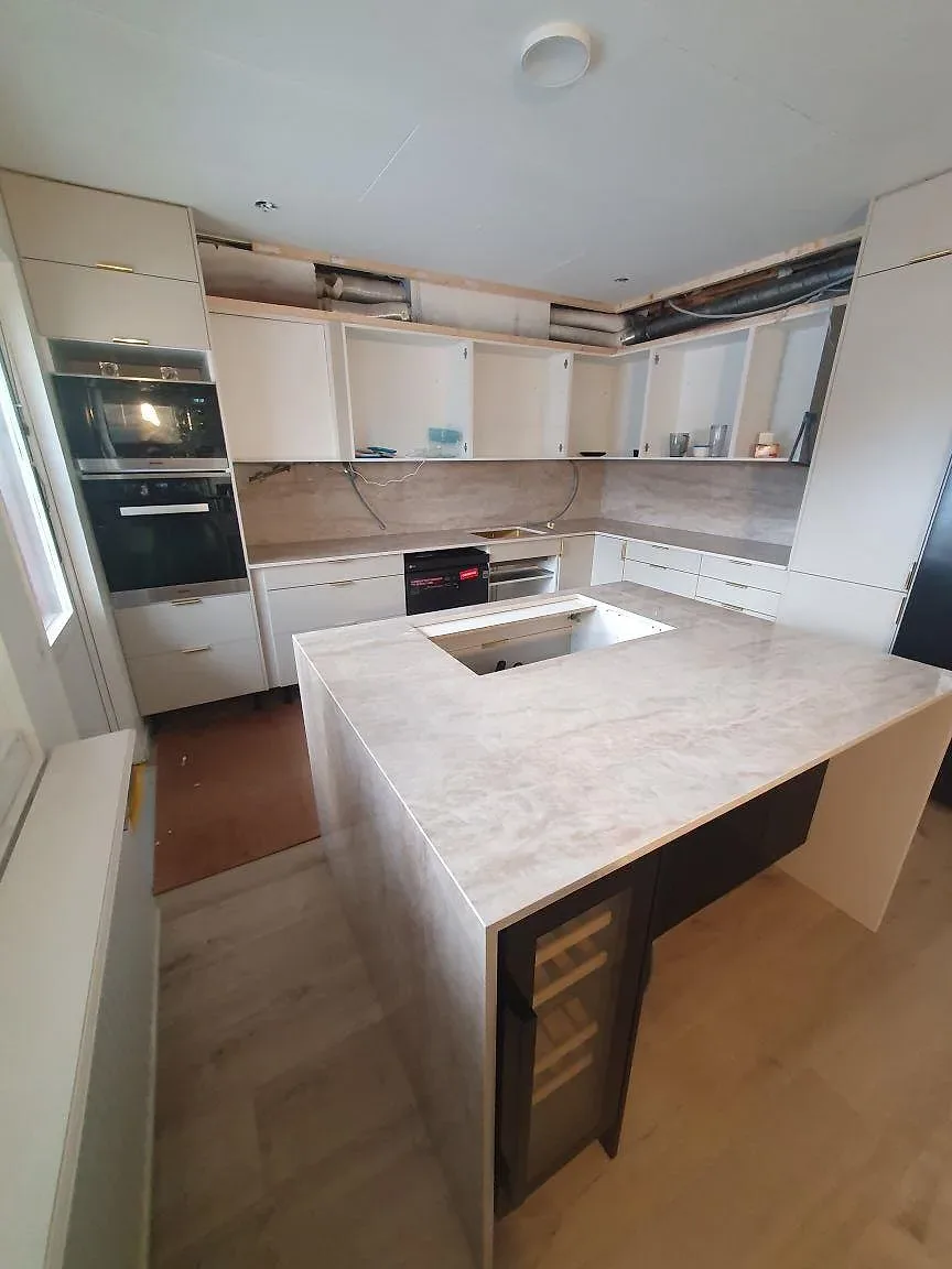 Polerad Dekton Arga köksö med hällurtag och intilliggande väggbänkar i ett kök under montering i Söderby.