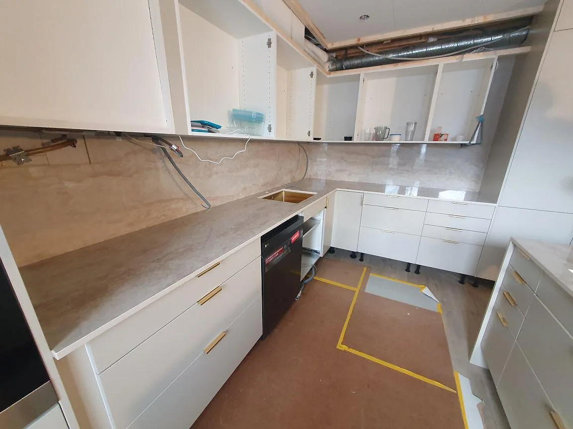 Väggbänk i polerad Dekton Arga keramik med diskho och stänkskydd mellan öppna skåp i Söderby.