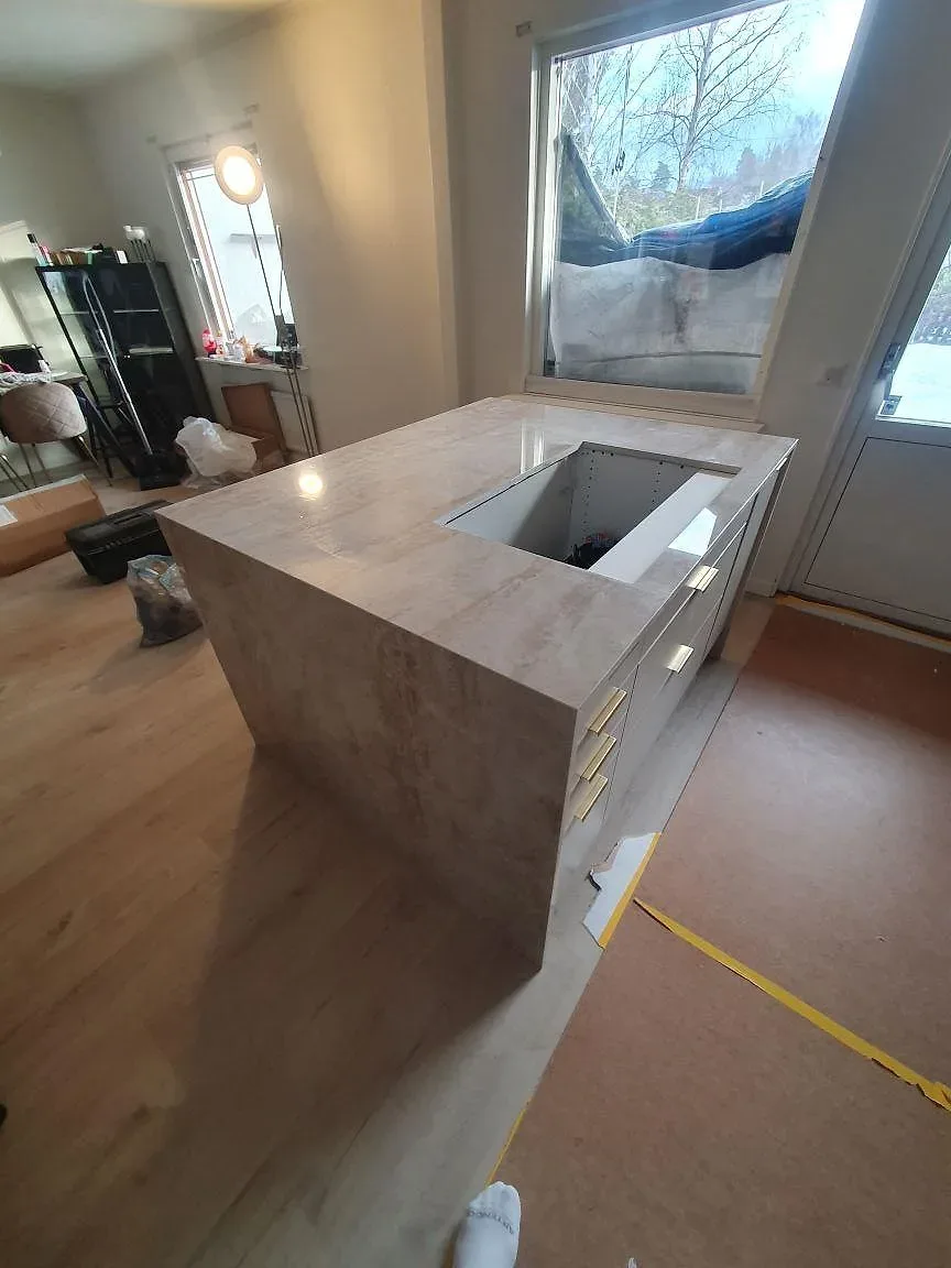 Detalj av köksö i polerad Dekton Arga keramik med hällurtag nära fönster och skyddat golv i Söderby.