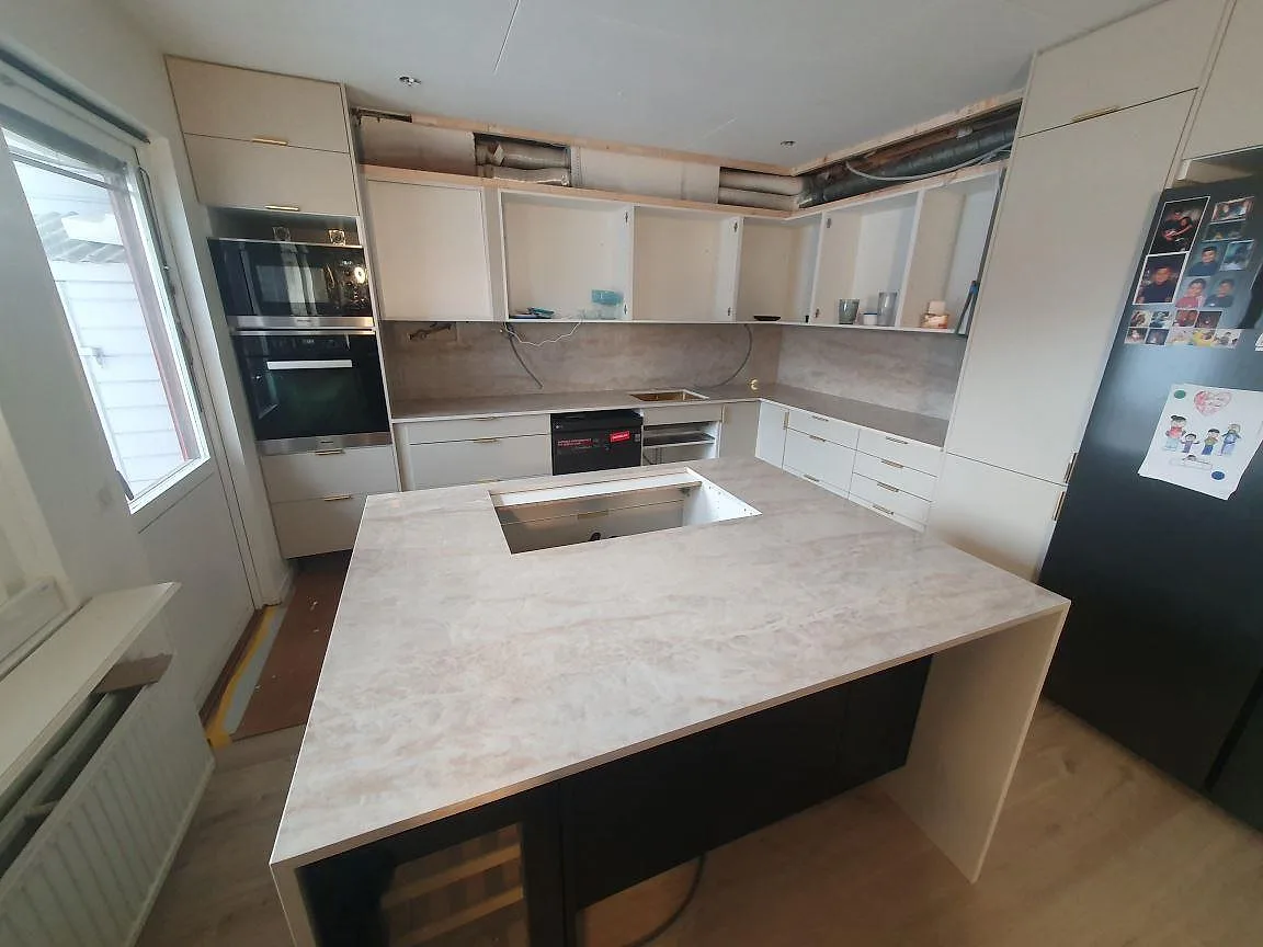 Köksbänkskiva och köksö i polerad Dekton Arga keramik med hällurtag och matchande stänkskydd i ett kök under montering i Söderby.