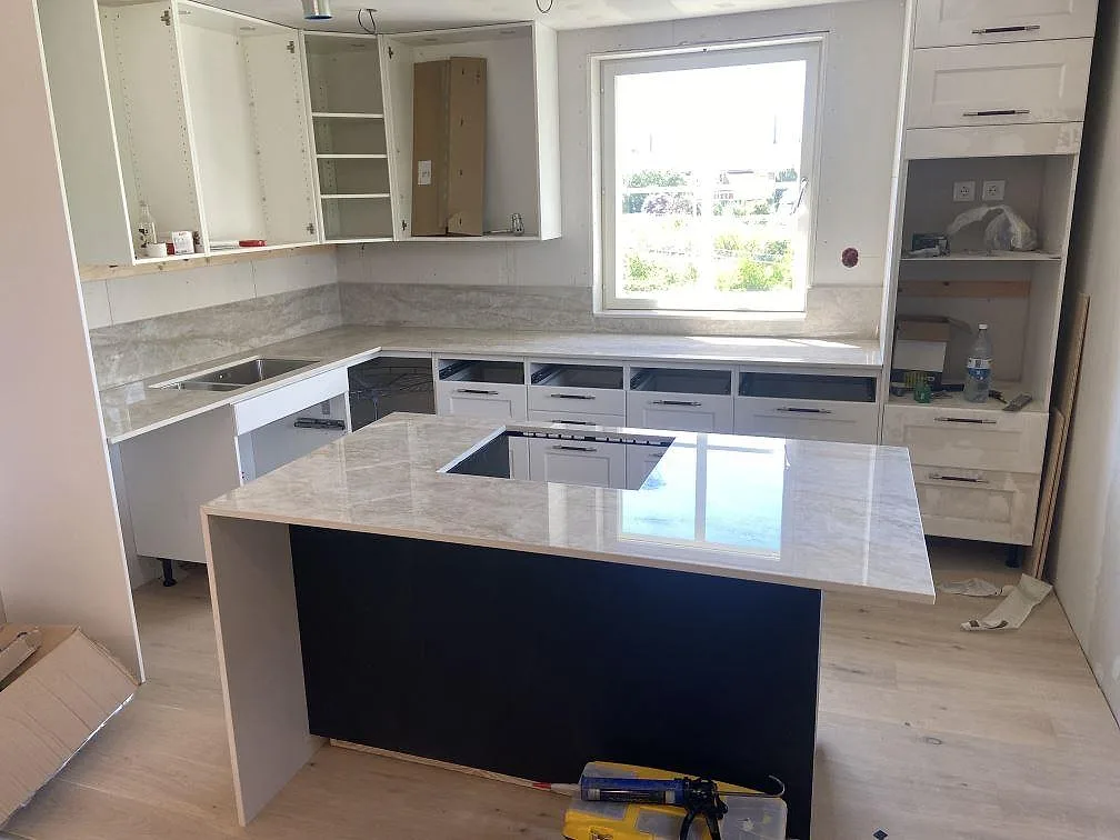 Köksbänkskiva och köksö i Dekton Arga, polerad krämvit keramik med brun-guldig ådring, med underlimmad diskho och infälld induktionshäll i ett kök i Sölvesborg.