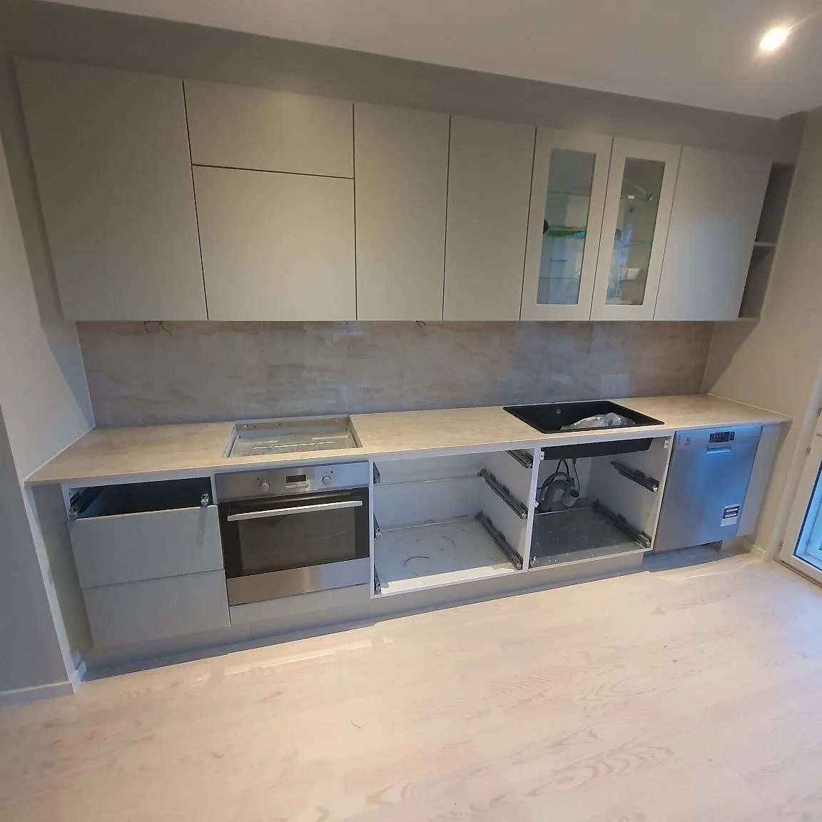 Köksbänkskiva i Dekton Arga keramik, polerad i varm cream, med matchande väggbeklädnad i ett kök under montering i Sollentuna.