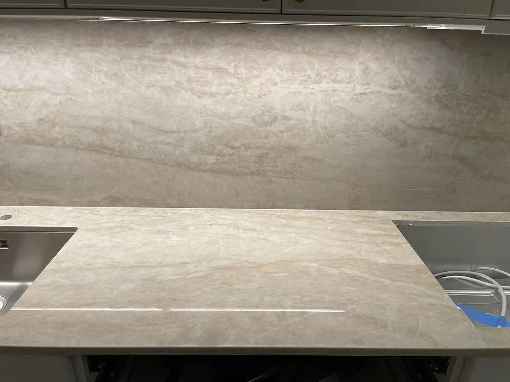 Polerad Dekton Arga köksbänkskiva med mjuk ådring, underlimmad rostfri diskho och heltäckande stänkskydd i ett kök i Solna.