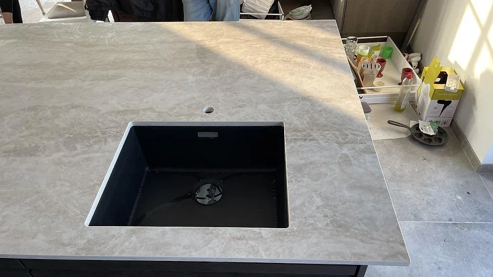 Detalj av polerad Dekton Arga, keramik, runt svart diskho och blandarhål i köket i Solrød.