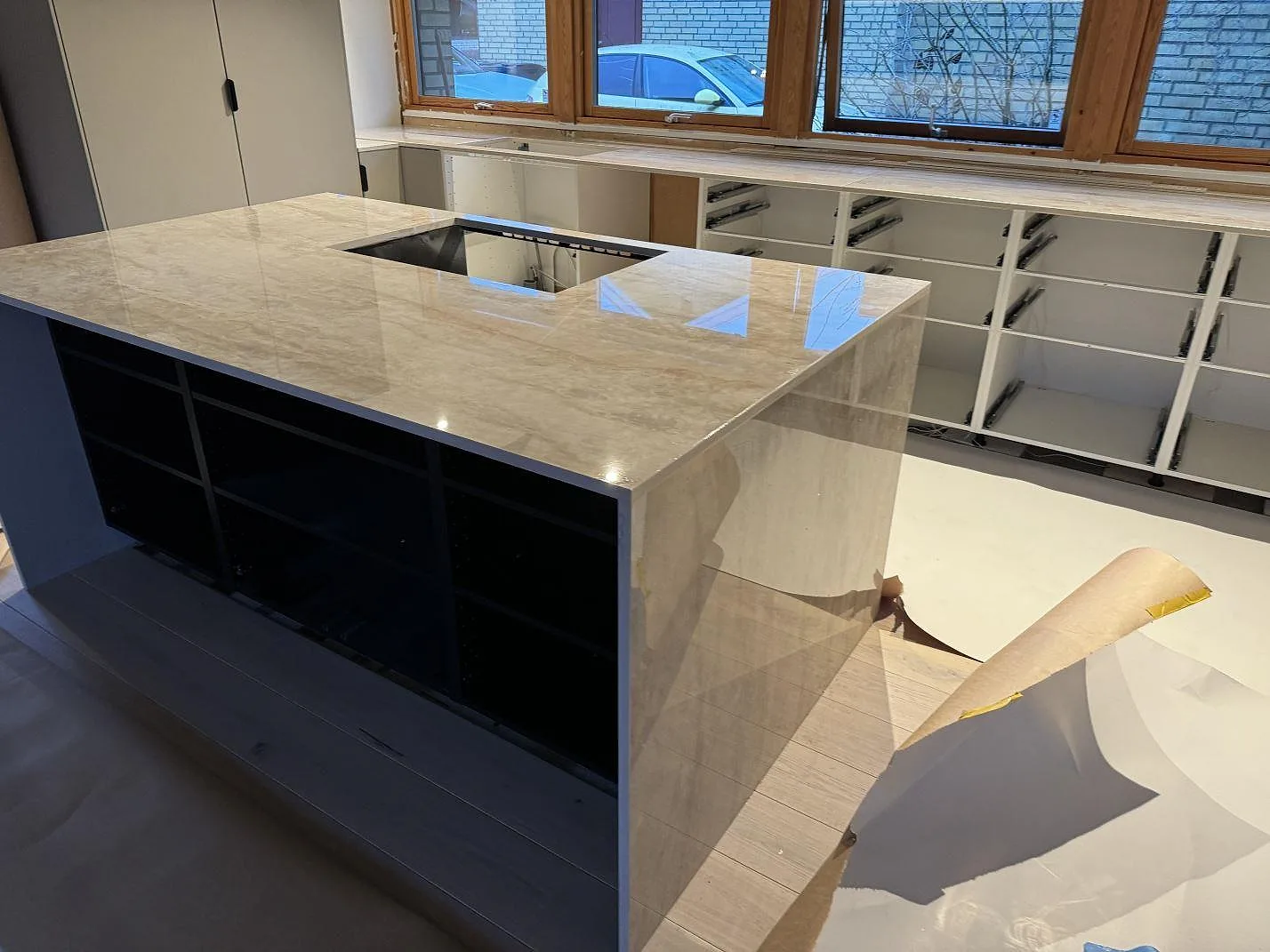 Köksö och köksbänkskiva i polerad Dekton Arga med hällöppning och träfönster i ett kök i Staffanstorp.