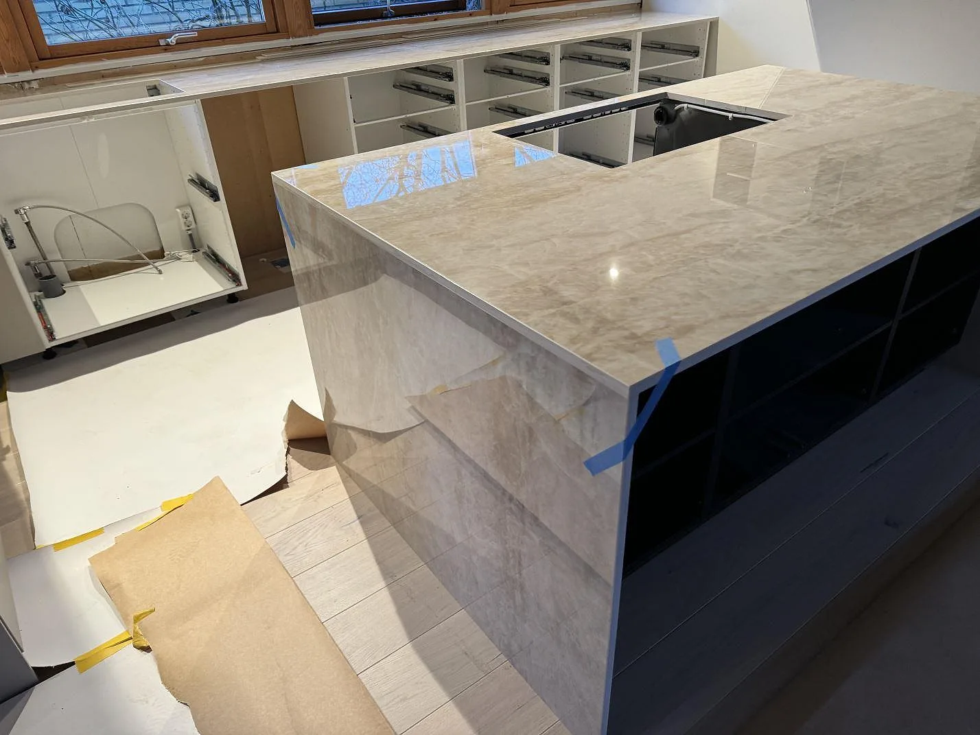 Närbild på köksö i polerad Dekton Arga med synlig ådring och pappersskydd på golvet i Staffanstorp.