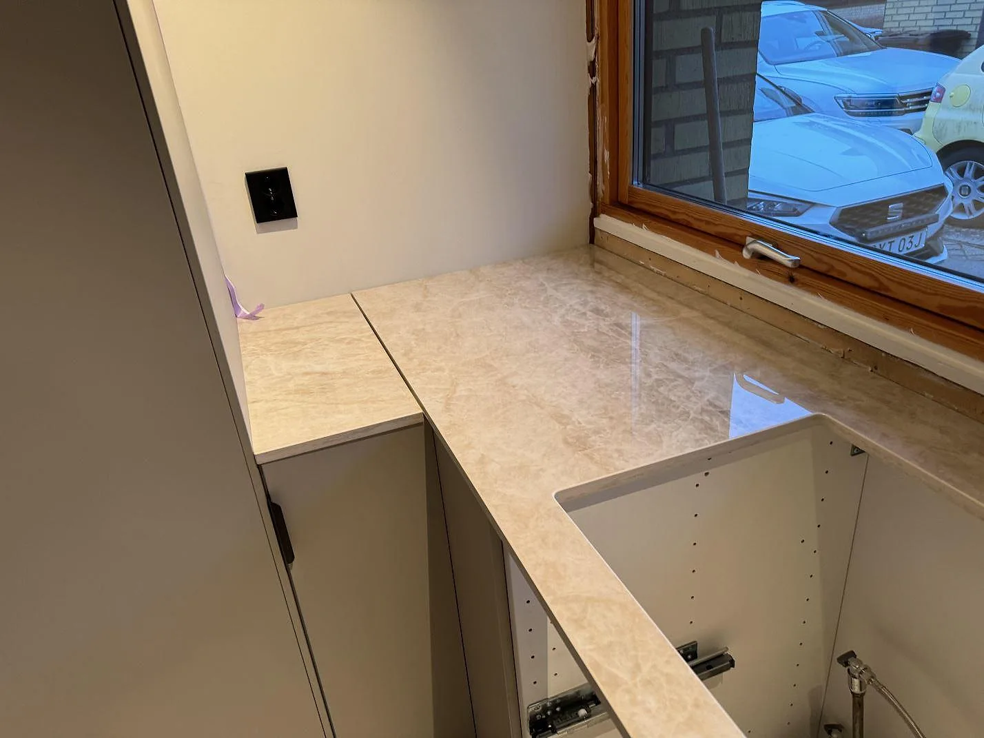 Hörn av köksbänkskiva i polerad Dekton Arga vid träfönster och öppen köksstomme i Staffanstorp.