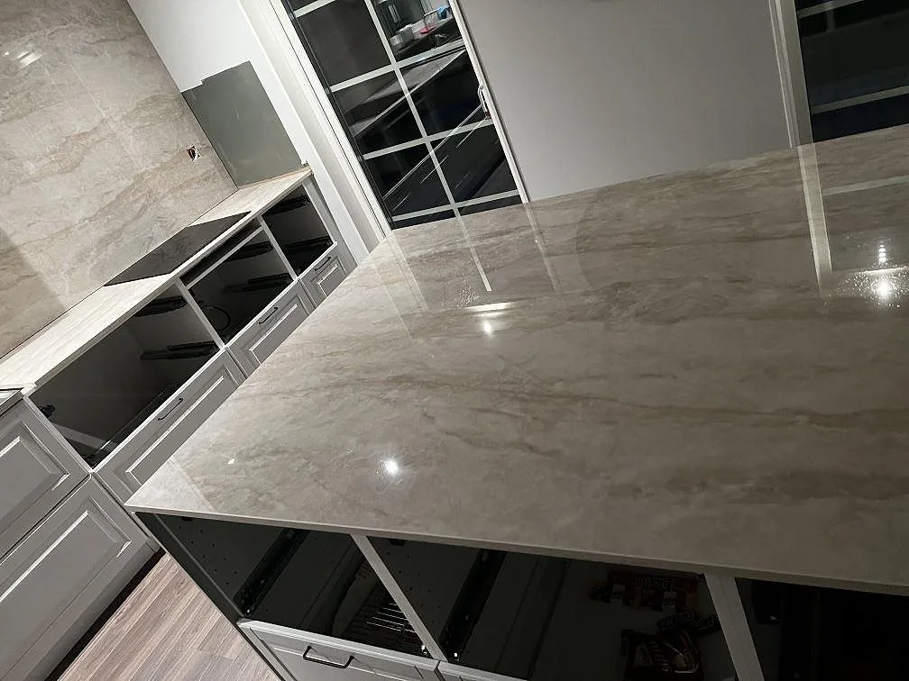 Vinklad vy över polerad Dekton Arga på halvö och väggbänk med hällplats och ljusreflexer i ett kök i Stenkullen.