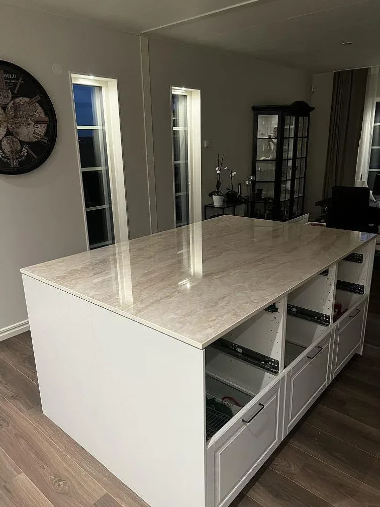 Polerad Dekton Arga som köksö med beigegrå ådring, vita stommar och mörka detaljer i ett kök i Stenkullen.