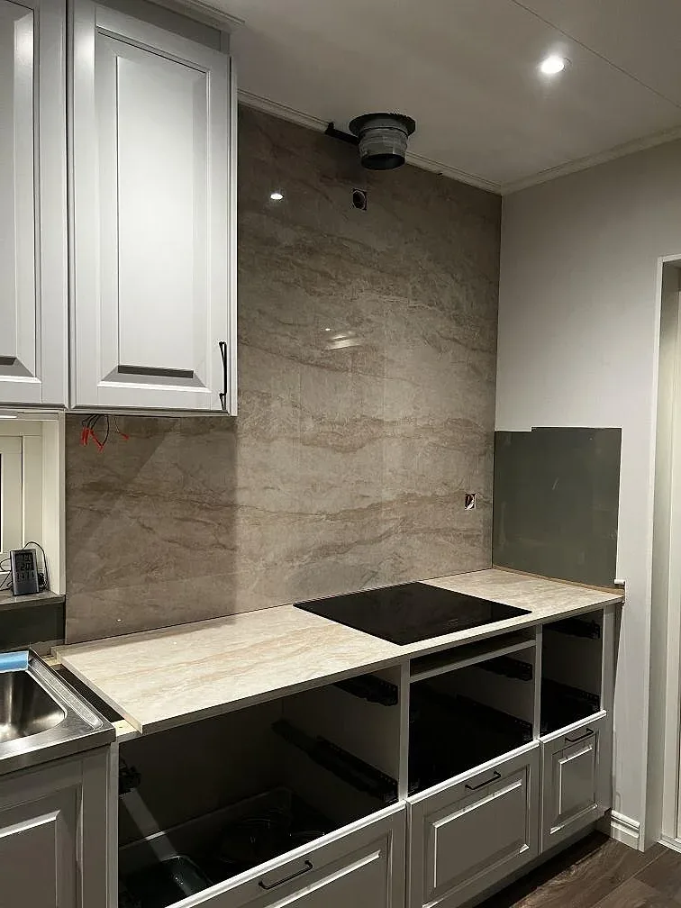 Köksbänkskiva i polerad Dekton Arga keramik med svart induktionshäll och hög stänkvägg i Stenkullen.